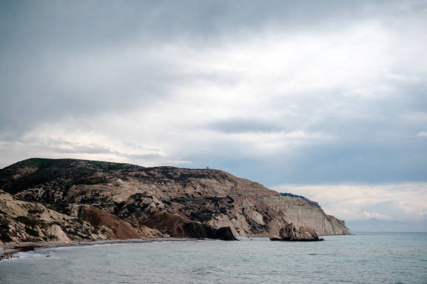 A scenic coastal landscape featuring rocky cliffs and a calm sea under a cloudy sky.