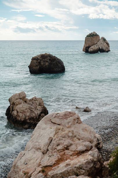 Rocky coastline with large boulders in the sea under a cloudy sky.
