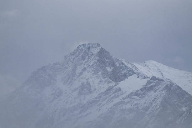 Mountain top is covered with snow in some places, through which the rock can be seen, the fog envelops the very top of the mountain