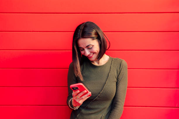 istock Smiling businesswoman using a smartphone with a red wall in the background 2191595870