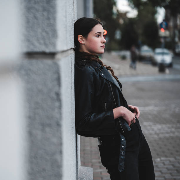 Young woman in a black leather jacket and boots posing confidently in an urban setting.