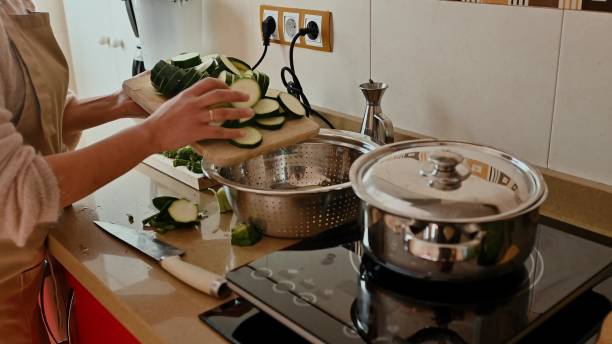 A person slices zucchini on a chopping board in a modern kitchen, preparing ingredients for a healthy recipe. The scene shows a countertop, cookware, and a focus on clean eating.
