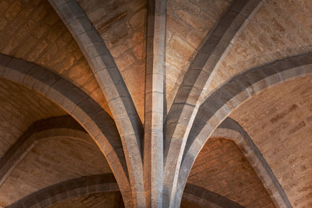 Intricate stone arches converge in a historic building, illuminated softly, showcasing craftsmanship.