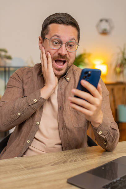 istock Happy young man freelancer using mobile phone celebrating success victory winning lottery at table 2191609898