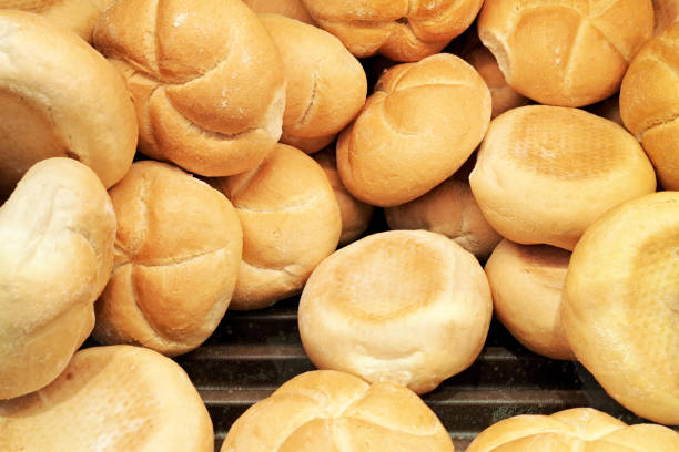 istock Fresh Kaiser rolls stacked on a store shelf. Group of classic bread rolls on display. Bakery section with a pile of golden brown buns. 2191615497