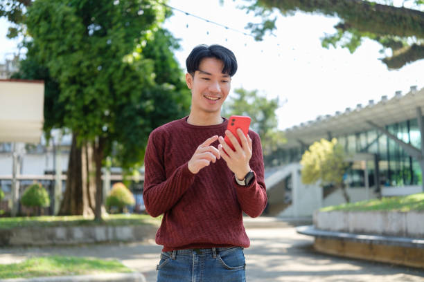 istock Smiling young man using smartphone outdoor with greenery and a modern building in background. 2191620314
