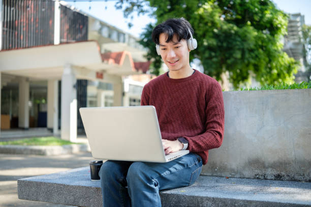 istock Young college student working on his laptop, studying outdoors while sitting on the steps in a campus park on a sunny day. 2191620318