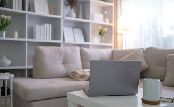 istock Minimalist home office setup featuring a laptop and coffee mug on a white table, with a comfortable beige sofa and stylish shelving in the background. 2191620715