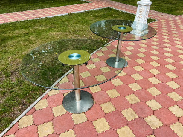 Two elegantly designed glass tables are meticulously arranged on a strong and durable brick sidewalk, forming a visually striking and appealing setup amidst the surrounding environment