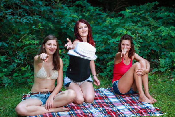 Three young woman having a great time in nature. Laughing and throwing straw hat into camera. Female friendship photo.