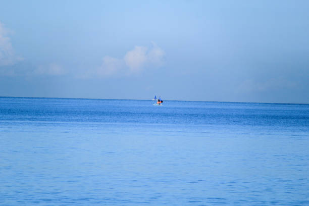 Two small sailboats with colorful sails float peacefully on calm, blue ocean waters. The vast expanse of the sea and a soft blue sky create a tranquil, minimalist composition.