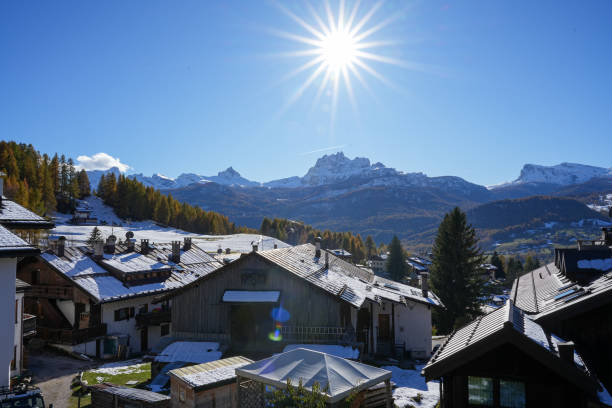 Charming alpine village under bright sun with snow-covered rooftops. Quaint rural houses amidst scenic mountains. Beautiful winter day in a sunlit mountain region.