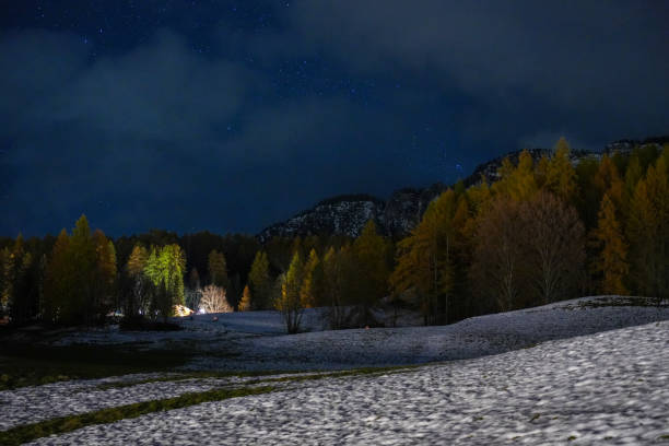 Picturesque village illuminated under a starry sky. Mountains provide a stunning backdrop. Perfect setting for a serene night landscape. Cozy lights of the village contrast the dark sky.