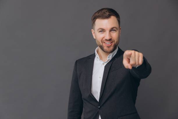 istock Caucasian millennial businessman isolated on gray studio background posing, smiling successful man in formal suit pointing finger and saying you on copy space 2191649146