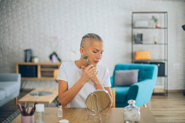 istock Middle aged woman improving her skin condition massaging her face with jade roller in front of a mirror at home 2191652967