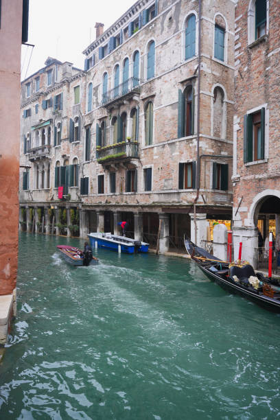 Scenic view of gondolas and boats navigating a narrow canal in Venice. Historic buildings with rustic charm line the waterway. Iconic Venetian architecture and waterways.