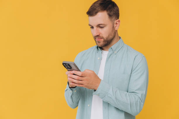 istock Happy unshaven young man using cell phone isolated on yellow background. Smiling hipster guy holding smartphone playing game in app, dating online, buying online in e commerce store on cellphone. 2191659960