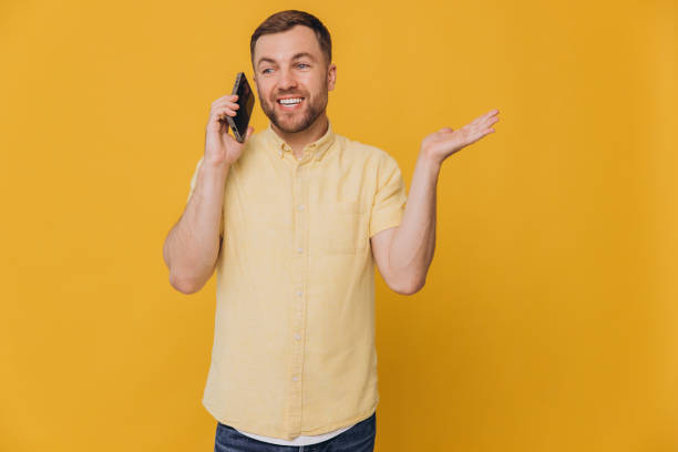 istock Handsome attractive smiling guy millennial hold phone and show copy space, popular blogger addicted user wear casual yellow shirt isolated yellow color 2191660429