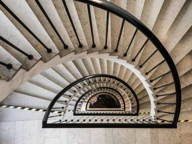 A stunning spiral staircase gracefully winds down through a contemporary building, featuring smooth steps and a sleek railing. The architectural design emphasizes elegance and symmetry.