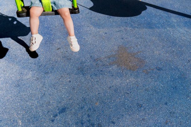 Close-up of a child’s feet wearing sneakers on a swing in a vibrant playground under the sun