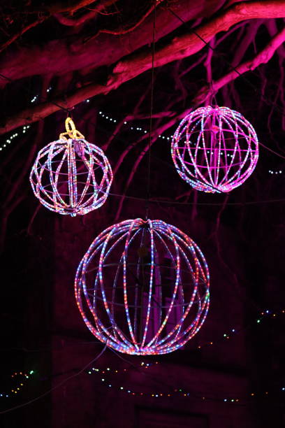 istock Christmas lights at night - large round multi coloured baubles hanging from a tree in a park 2191673639