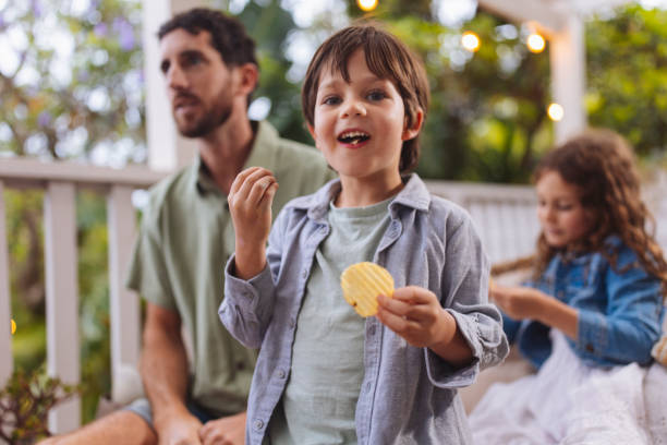 Boy enjoying snack Young boy eating chips with his family in the background family eating potato chips stock pictures, royalty-free photos & images