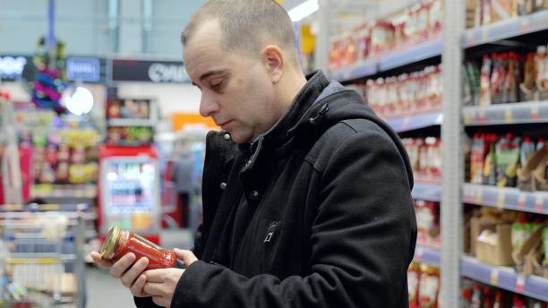 istock Health conscious shopper reading product label, comparing nutrition facts while selecting groceries in supermarket aisle 2191680444