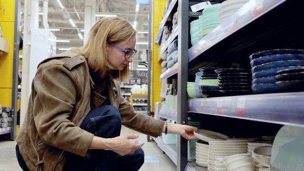 istock Woman selecting plates in a supermarket houseware section, holding a white plate and browsing the shelves 2191680646