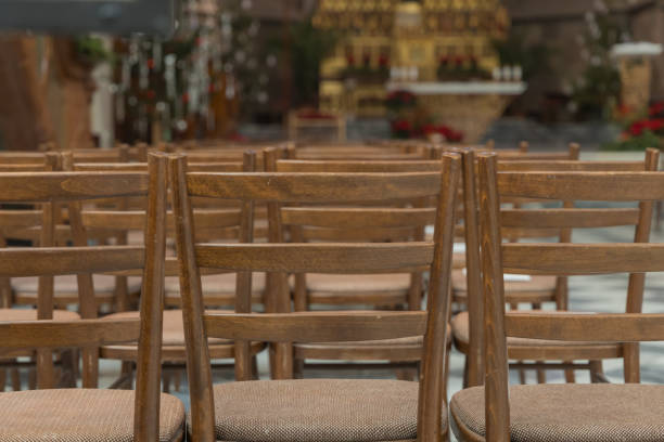 A row of empty wooden pews inside a Catholic church, leading towards an ornate altar, creating a peaceful and sacred atmosphere. Church Parròquia de Sant Ramon de Penyafort in Barcelona, Spain.