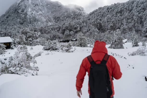 istock A man wearing a red jacket and black backpack is walking through the snow 2191691035