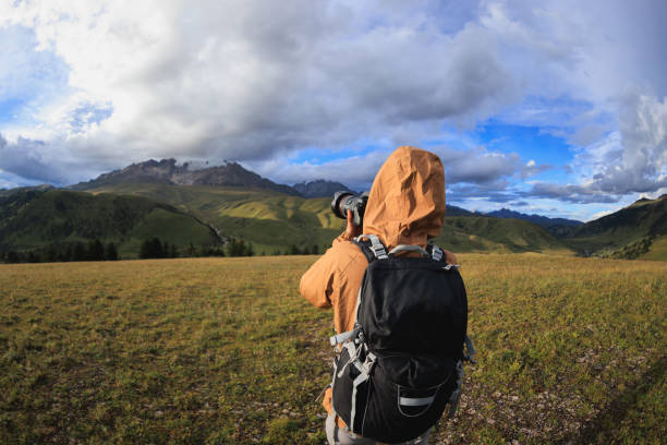 Woman backpacker hiking on high altitude mountains taking picture of  the snow capped mountain in the distance