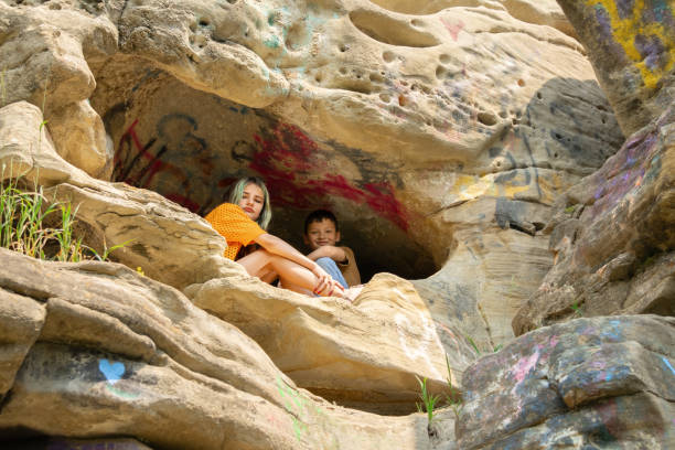 Two teenagers, a boy and a girl with green hair, sitting in a cave covered with graffiti on a cliff in summer. Escape place to hide. Gundy caves, British Columbia, Canada.