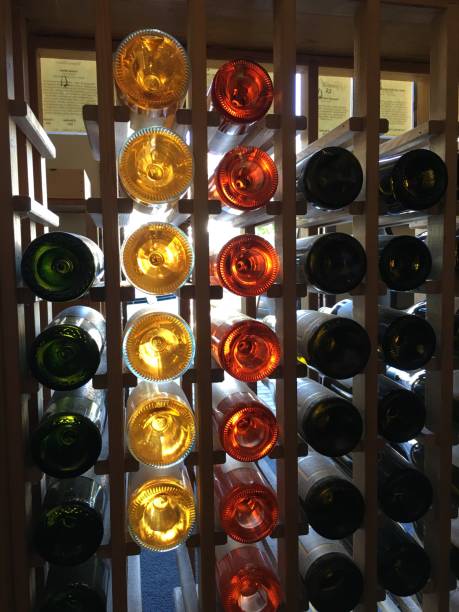 The back side of wine bottles, arranged horizontally in a wooden rack. The vibrant colors of green, yellow, and red bottles create a visually appealing pattern.