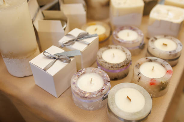 A table with candles and boxes of candles. The candles are in various shapes and sizes, and the boxes are white. Scene is calm and relaxing, as candles are often associated with relaxation