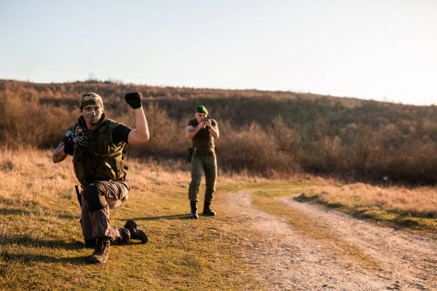 Two individuals in military gear performing tactical exercises in an open field during daylight. The scene depicts action and teamwork, emphasizing outdoor training activities in a strategic environment suitable for military or survival scenarios.