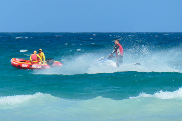On the left, two volunteer lifesavers of Surf Life Saving Australia patrol in an inflatable boat off Bondi Beach, Sydney. On the right is a Waverley Council lifeguard patrolling on a jet ski and trailing a floatation mattress for assisting swimmers in trouble. This image was taken from the southern end of the beach on a hot and sunny afternoon on 29 December 2024.