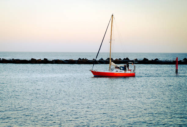 A seascape with a red stylish yacht at sunset sails across the Atlantic Ocean, into the bay during its sea voyage.