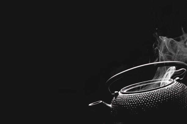 Rustic tea pot on black background. Steaming teapot. Cooking concept.