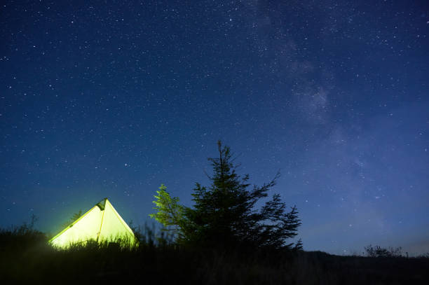 istock Glowing yellow tent stands under vast, starry sky, with Milky Way. 2191745150