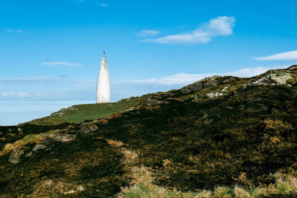 istock A modern, white tower-like object is situated on a hill. The hill's surface is uneven, with exposed rocks and patches of grass. The day is sunny. 2191747070