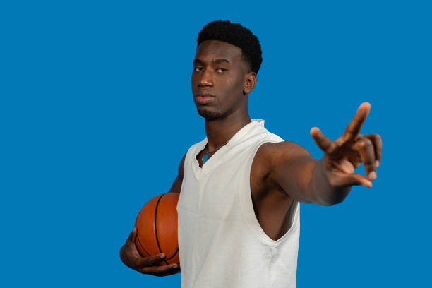 Young athlete spinning a basketball on his fingertip, showcasing skill and concentration against a vibrant blue backdrop