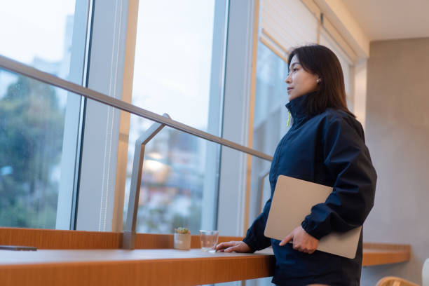 istock asian female holding laptop while standing  beside window and look away 2191753092