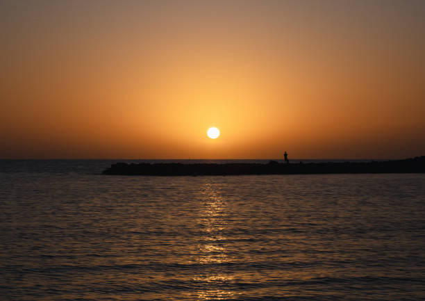 This breathtaking image captures the stunning sunset at Adeje Coast in Tenerife. The sky is ablaze with vibrant hues of orange, pink, and purple, reflecting off the calm waters of the Atlantic Ocean. The silhouette of the rugged coastline and cliffs adds depth and drama to the scene, enhancing the natural beauty of the setting sun. The warm glow of the sunset bathes the landscape in a soft, golden light, creating a tranquil and mesmerizing atmosphere. Ideal for travel and nature photography stock, this image perfectly encapsulates the serene and picturesque beauty of a sunset at Adeje Coast, making it a perfect choice for capturing the essence of Tenerife's coastal charm.