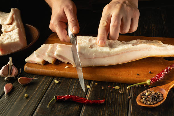 istock Hands skillfully cut through succulent pork belly on a wooden board, surrounded by vibrant spices and garlic. The warm ambiance of the kitchen enhances this culinary moment 2191755307