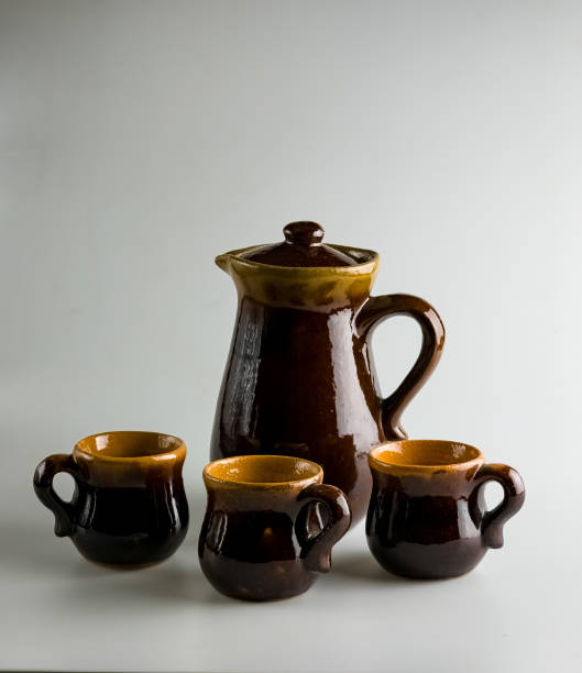 Ceramic dishes on a white background, a clay teapot and three cups. Vertical photo.