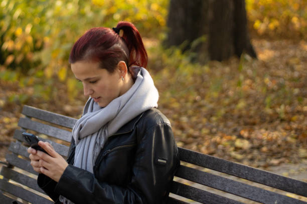 istock woman sitting on bench using smartphone in park 2191758559