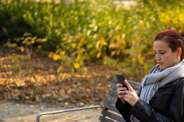 istock woman sitting on bench using smartphone in park 2191758568