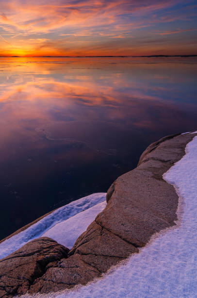 istock Vibrant sunset reflection over calm waters with snow-covered rocks in the foreground 2191765075