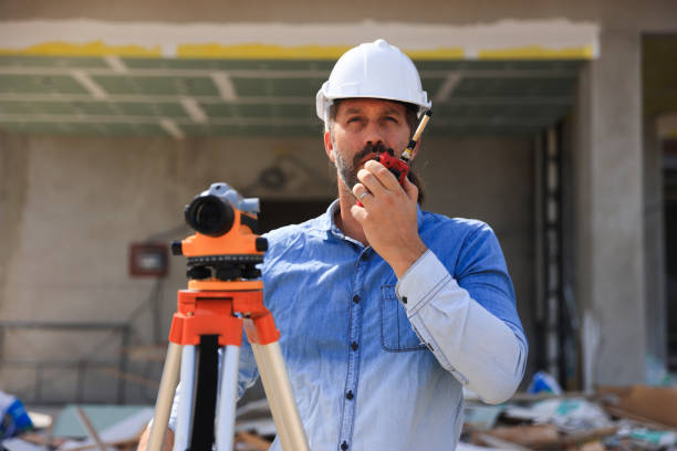 Surveyor with walkie-talkie looking through measuring level on construction site