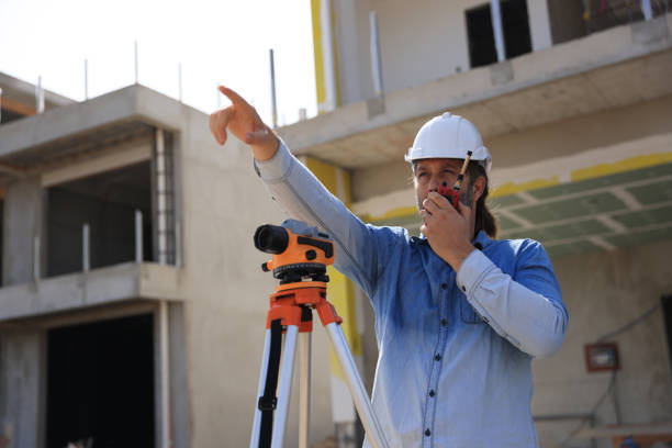 Surveyor with walkie-talkie looking through measuring level on construction site